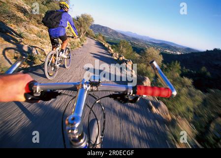 Due uomini in bicicletta, vista dalla bicicletta dietro, strada vicino Castell Alaro, Tramuntana, Maiorca, Spagna Foto Stock