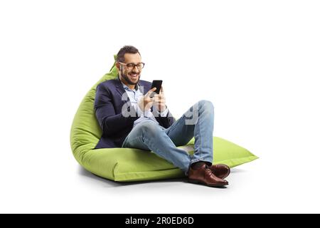 Giovane professionista seduto su una borsa di fagioli sorridendo e guardando uno smartphone isolato su sfondo bianco Foto Stock
