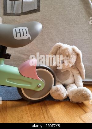 Equilibrare la ruota della bicicletta e un giocattolo. Coniglio giocattolo e una bicicletta per bambini. Tenda da teepee sullo sfondo. Sala giochi per bambini. Foto Stock