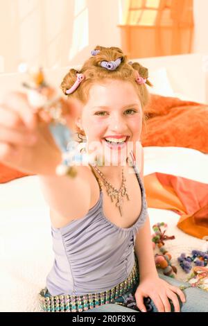 Ragazza adolescente (14-16) seduta a letto e ridendo Foto Stock