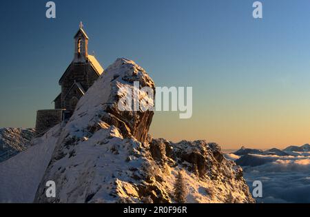 Cappella coperta di neve sulla formazione rocciosa all'alba, Wendelstein, Bavarese Range, alta Baviera, Germania Foto Stock