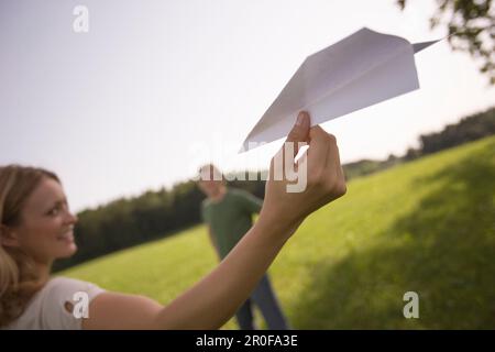 Giovane donna che lancia aeroplano di carta sul prato Foto Stock