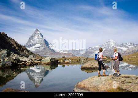 Due escursionisti femminili che guardano il riflesso della faccia orientale, Hoernlivrat, del Cervino, 4478 m, a Riffelsee, Zermatt, Vallese, Svizzera Foto Stock