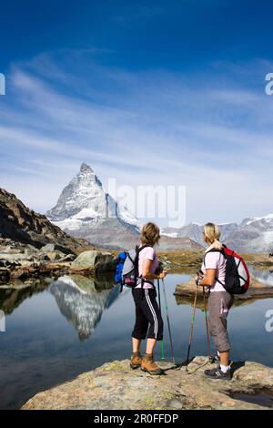 Due escursionisti femminili che guardano il riflesso della faccia orientale, Hoernlivrat, del Cervino, 4478 m, a Riffelsee, Zermatt, Vallese, Svizzera Foto Stock