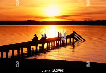 Persone sul molo al Lago Starnberg al tramonto, St Heinrich, alta Baviera, Baviera, Germania Foto Stock