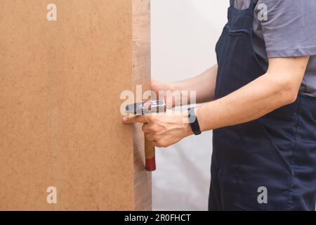 Servizi specializzati di assemblaggio e riparazione di mobili martellando i reggimensola in un armadio in legno Foto Stock