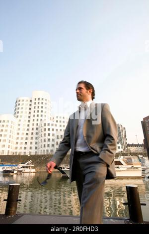 Giovane uomo d'affari che cammina attraverso Media Harbour, di fronte all'architettura moderna di Frank Gehry, gli uffici, Düsseldorf, capitale dello stato della NRW Foto Stock