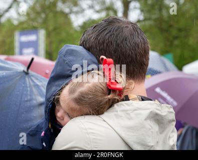 Giovane ragazza che riposa sulle spalle (presunte) del padre durante le precipitazioni a Hyde Park mentre osserva l'incoronazione di Re Carlo III sugli schermi Foto Stock