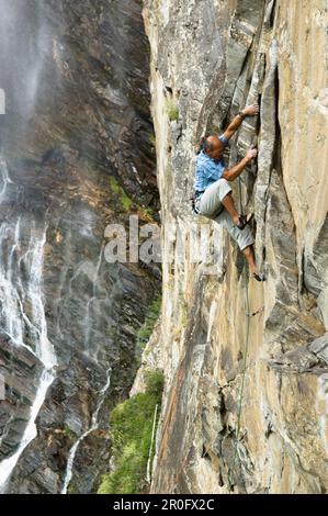 Uomo arrampicata su roccia a Maltatal, cascata sullo sfondo, cascata Fallbach, Parco Nazionale Tauern, Carinzia, Austria Foto Stock