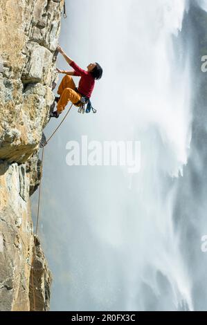 Parete rocciosa di scalata libera femminile, cascata Fallbach sullo sfondo, Valle di Malta, Parco Nazionale Hohe Tauern, Carinzia, Austria Foto Stock