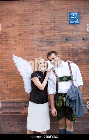 Angel, giovane donna con ali in piedi accanto ad un uomo in abito tradizionale, Monaco, Baviera, Germania Foto Stock