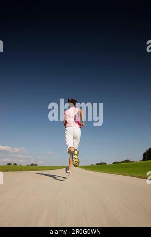 Donna jogging lungo strada, Munsing, Baviera, Germania Foto Stock