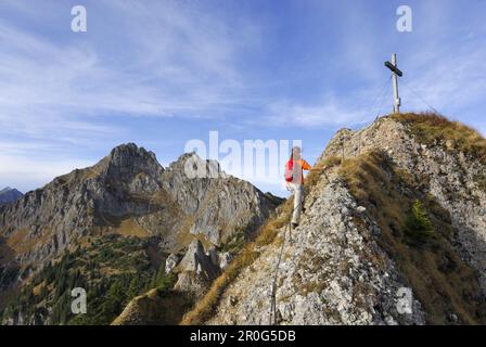 Donna che sale verso la croce sommitale di Brunnenkopf, Alpi Ammergau, Pfaffenwinkel, Baviera, Germania Foto Stock