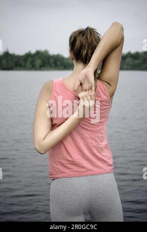 Giovane donna che si estende sul lago di Starnberg, Baviera, Germania Foto Stock