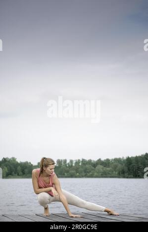 Giovane donna stretching su un molo al lago di Starnberg, Baviera, Germania Foto Stock