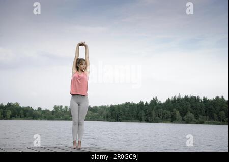 Giovane donna stretching su un molo al lago di Starnberg, Baviera, Germania Foto Stock