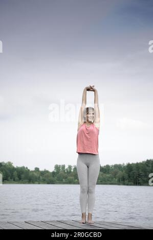 Giovane donna stretching su un molo al lago di Starnberg, Baviera, Germania Foto Stock