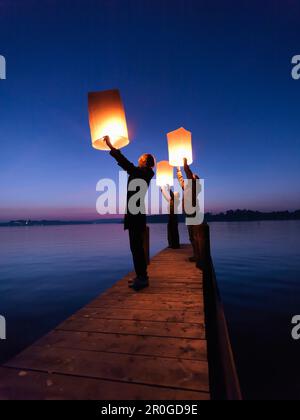 Tre persone che detengono lanterne Sky, Lago di Chiemsee, Baviera, Germania Foto Stock
