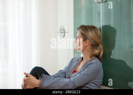 Donna media adulta che guarda fuori da una finestra Foto Stock