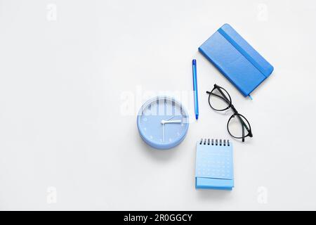 Calendario a fogli mobili, sveglia, occhiali e notebook su sfondo blu Foto Stock