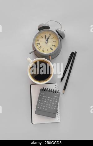 Calendario a fogli mobili con sveglia e tazza di caffè su sfondo grigio Foto Stock