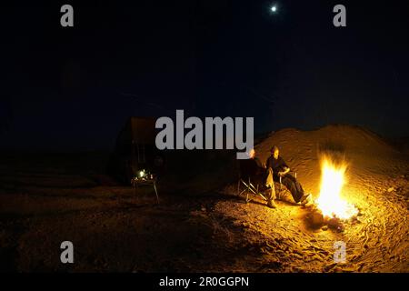 Coppia seduta accanto al fuoco a luna piena, Chott El Jerid, Douz dune, Tunesia, Africa Foto Stock