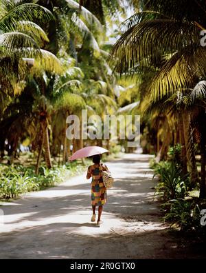 Donna che cammina attraverso la piantagione di alberi di cocco l'Union Estate, la Digue, la Digue e Inner Islands, Repubblica delle Seychelles, Oceano Indiano Foto Stock