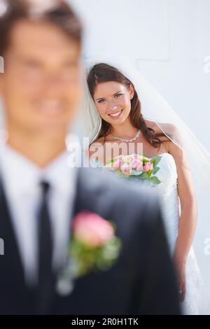 Si trova dietro di lui. Una splendida sposa sorridente felicemente mentre suo marito-da-essere è in piedi sfocato in primo piano. Foto Stock