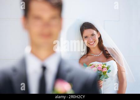 Dietro ogni uomo buono c'è una donna. Una splendida sposa sorridente felicemente mentre suo marito-da-essere è in piedi sfocato in primo piano. Foto Stock