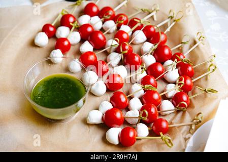 Delizioso antipasto Caprese Canapes sugli spiedini. Un antipasto colorato su spiedino, con mozzarella fresca e pomodori ciliegini, servito su un letto di carta W. Foto Stock