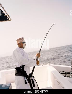 OMAN, Moscato, giovane uomo in abbigliamento tradizionale la pesca in barca Foto Stock