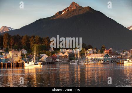 ALASKA, Sitka, una vista tranquilla di case e barche da pesca lungo la riva del porto di Sitka al tramonto, Monte Verstovia picco in lontananza Foto Stock