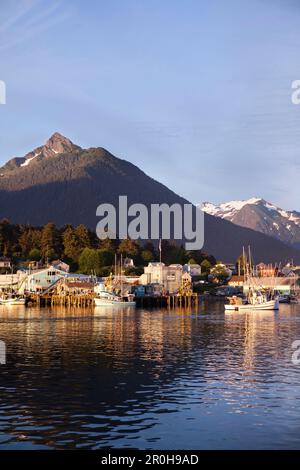 ALASKA, Sitka, una vista tranquilla di case e barche da pesca lungo la riva del porto di Sitka al tramonto, Monte Verstovia picco in lontananza Foto Stock