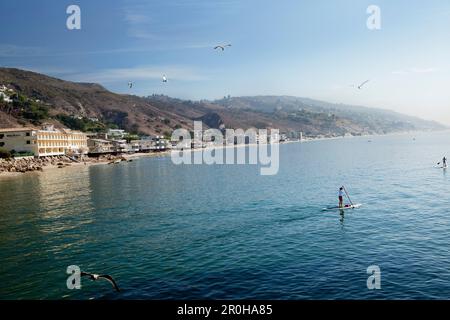 USA, California, Malibu, paddleboarders crociera dal molo di Malibu con il Malibu Beach Inn in lontananza Foto Stock