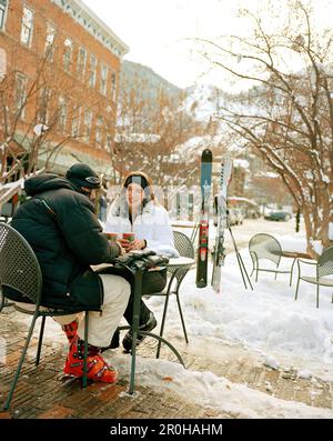 USA, Colorado, Aspen, coppia che indossa l'attrezzatura da sci e che ha un caffè al tavolo all'aperto in inverno, nel centro città Foto Stock