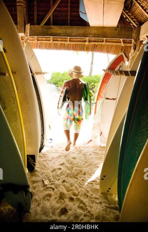 INDONESIA, Isole Mentawai, Kandui Resort, vista posteriore di un uomo che porta tavole da surf fuori dal magazzino Foto Stock