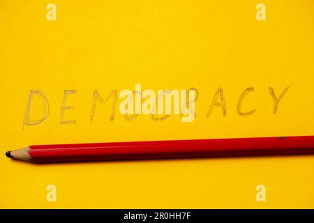 La parola democrazia scritta a matita su sfondo giallo. Foto Stock