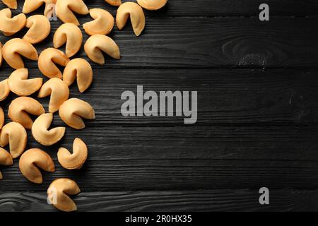 Biscotti gustosi della fortuna con predizioni su tavolo di legno nero, piatto. Spazio per il testo Foto Stock