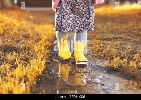 Bambina che indossa stivali di gomma camminando in pozza all'aperto, primo piano Foto Stock