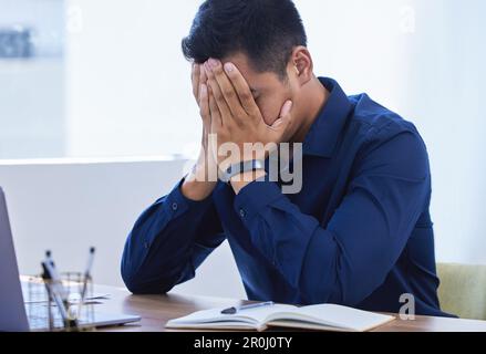 Non un altro giorno cupo... un giovane uomo d'affari che guarda stressato mentre lavora in un ufficio. Foto Stock