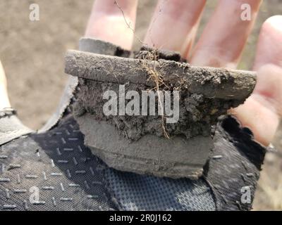 Un frammento di un antico recipiente in ceramica che si trova nel terreno si trova nel palmo della mano Foto Stock