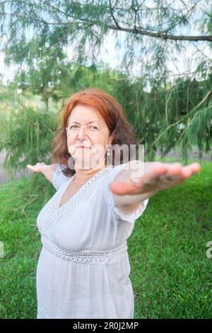 Ritratto di una donna ispanica matura in abiti bianchi praticando yoga all'aperto in un parco. Concetti: Benessere, vitalità, stile di vita attivo e sano. Foto Stock