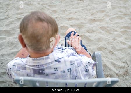 Vista posteriore e superiore di un anziano asiatico seduto su una sedia. Fuoco selettivo sulla sua mano. Concetto di invecchiamento. Foto Stock