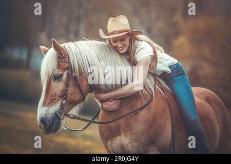 Una giovane donna bionda e il suo cavallo haflinger che si divertono in primavera all'aperto. Scena di amicizia tra una donna equestre e il suo pony Foto Stock