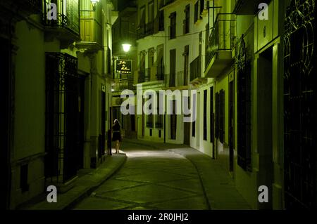 Lonesome donna che cammina di notte in un vicolo scarsamente illuminato con luce verde a Priego de Cordoba, Sierra Subeticas, provincia di Córdoba, Andalusia, Spagna Foto Stock