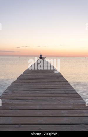 Donna che cammina lungo un lungo molo in umore di mattina. Playa de Muro, Alcudia, Maiorca, Isole Baleari, Spagna Foto Stock