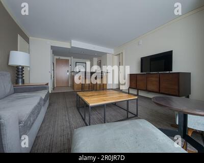 Suite business vuota con tv a schermo piatto, divano, tavolo in legno, sgabelli da bar Foto Stock