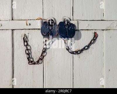 Serrature rustiche in metallo con catena su una porta di legno bianco Foto Stock