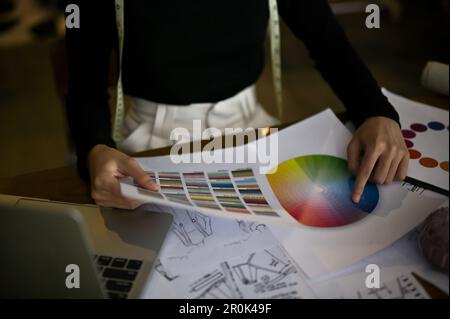 Immagine ravvicinata di una fashion designer professionista che sceglie il colore da una tabella dei campioni di colore, lavorando nel suo studio. Foto Stock