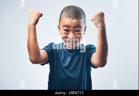 Posso fare tutto ciò che ho in mente. Studio shot di un ragazzino carino che flette i muscoli su uno sfondo grigio. Foto Stock